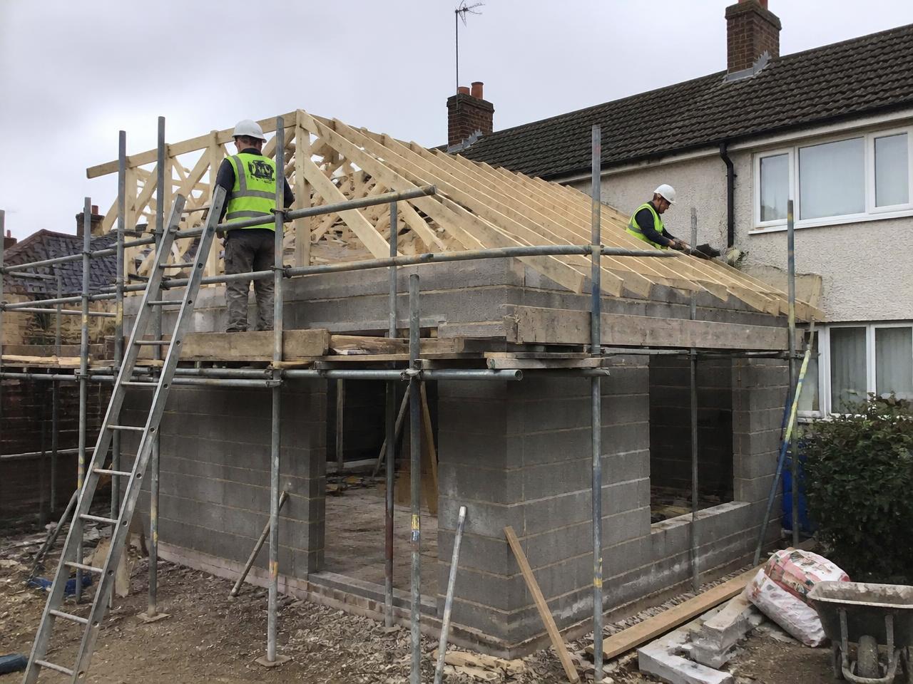 Builders working on the blockwork and roof timbers of a single storey house extension.